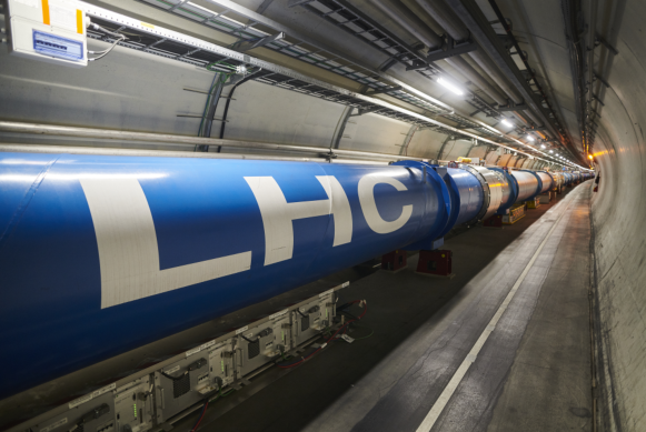 Figure shows image a of a long tube and its surrounding tunnel used in a particle collider.