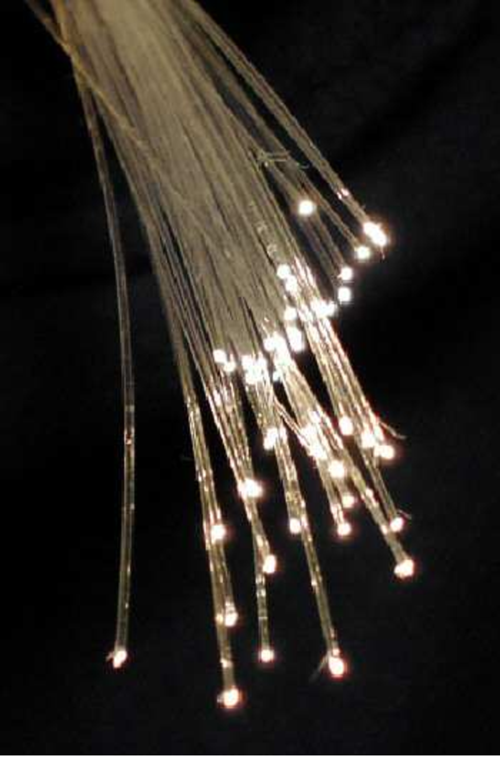 A bundle of clear, thin strands of fiber in a dark background. The tips of the fibers are glowing with white light.