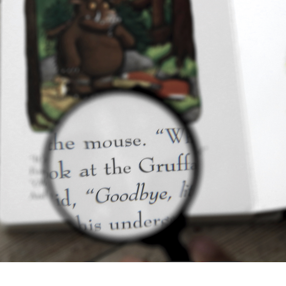 A handheld magnifying glass enlarges words and an illustration on a children's book page.