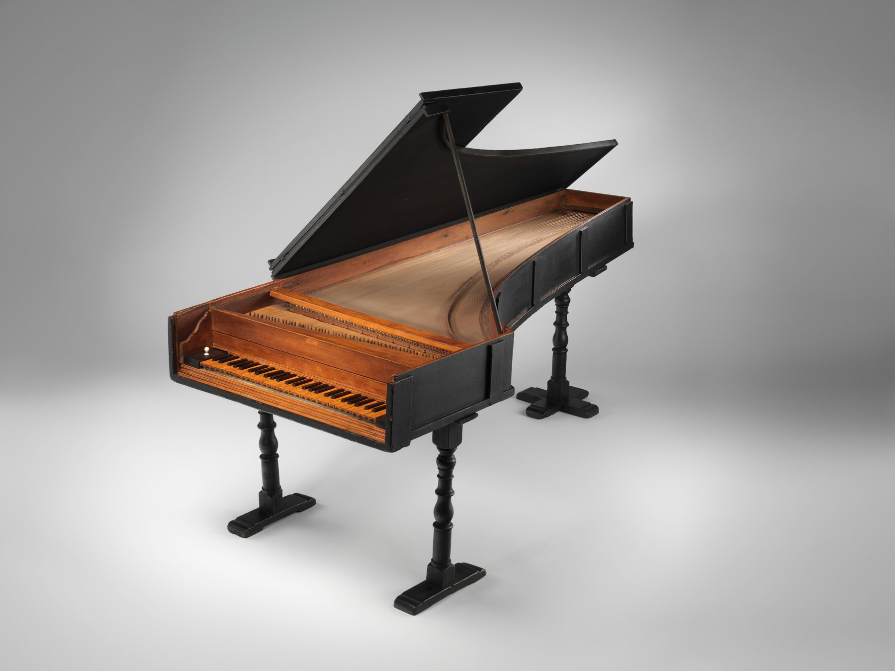 An early grand piano photographed in a museum collection, its lid raised to show the case and legs.