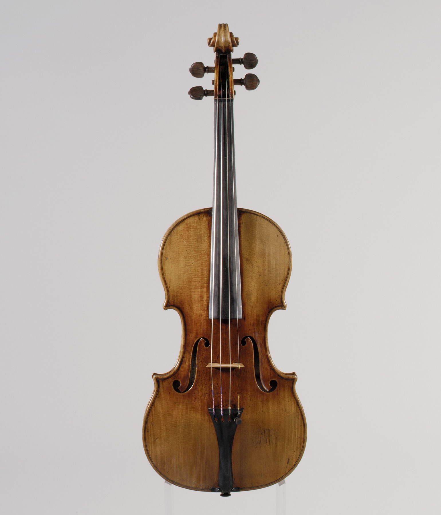 The front of a violin photographed against a neutral background, showing the body, f-holes, bridge, strings, and scroll.